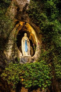 Luminous Virgin Mary statue at the Lourdes Grotto in natural rock setting.